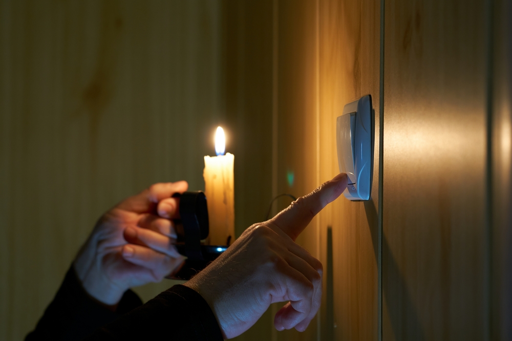 A man with a burning candle in his hand turns a light switch on and off. Blackout no electricity light, power outage, systemic accident in power system accompanied by mass disconnection of consume
