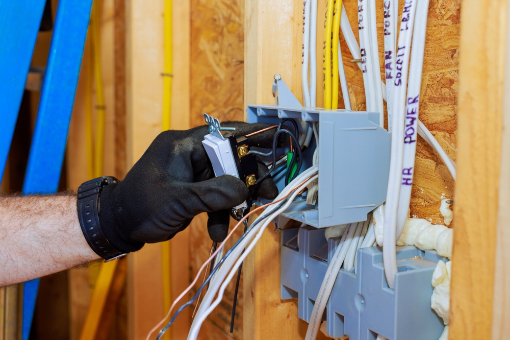 An electrician connects wires to switch in junction box in home being built, prioritizing safety