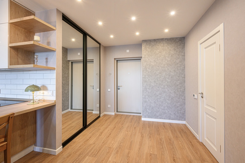 Recessed lighting inside residential home with hardwood floors, grey walls, wooden shelves, and mirrors